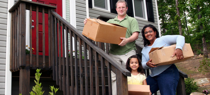 Interacial couple and child carrying moving boxes into their new home.