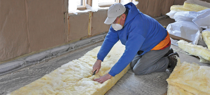 Workman laying insulation in room of house.
